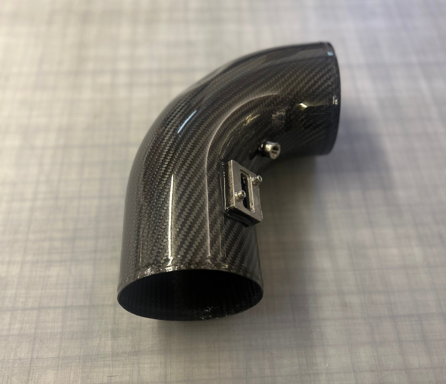 Carbon fiber intake pipe on a gray grid background