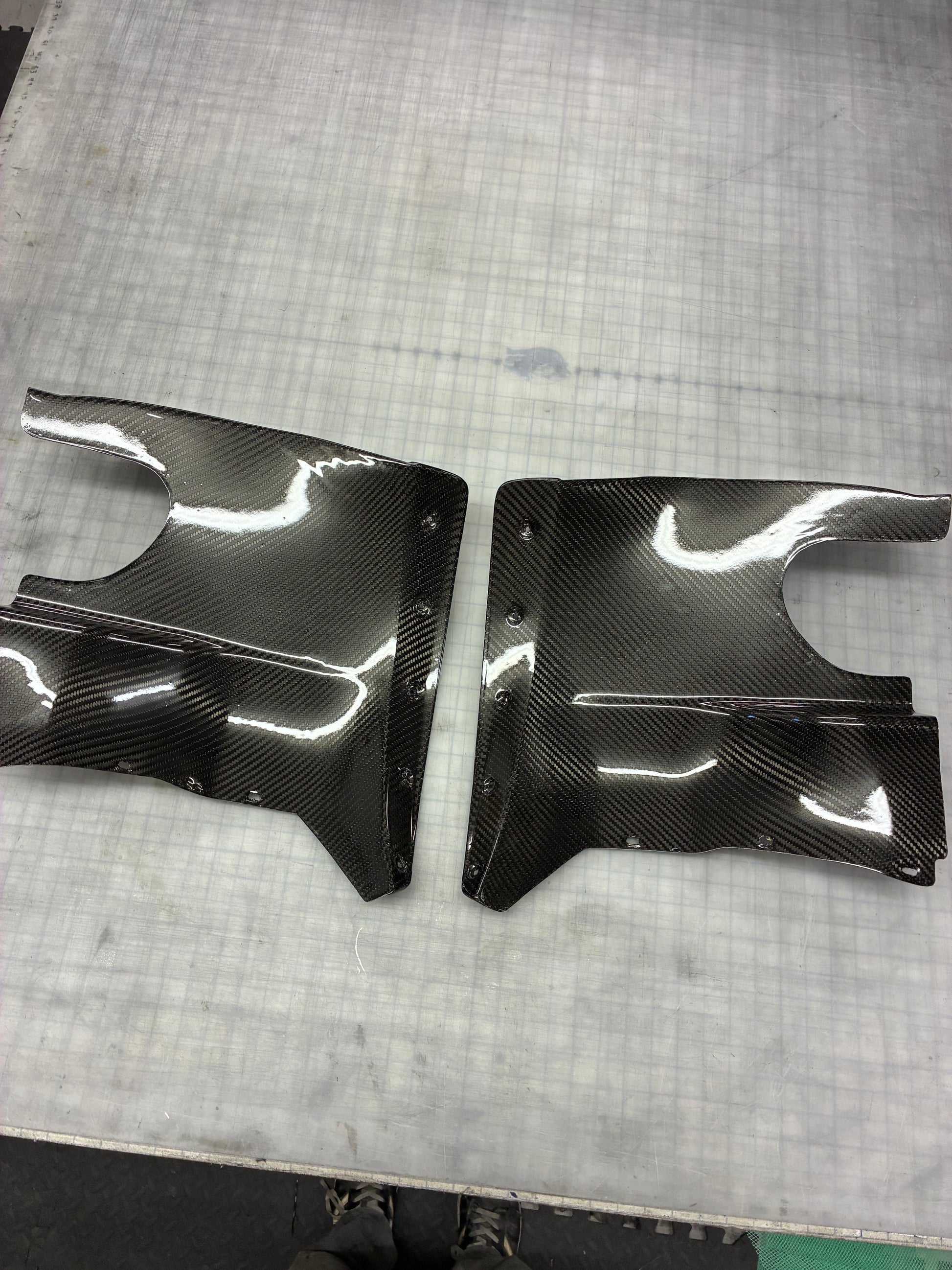 Two carbon fiber car parts on a textured surface