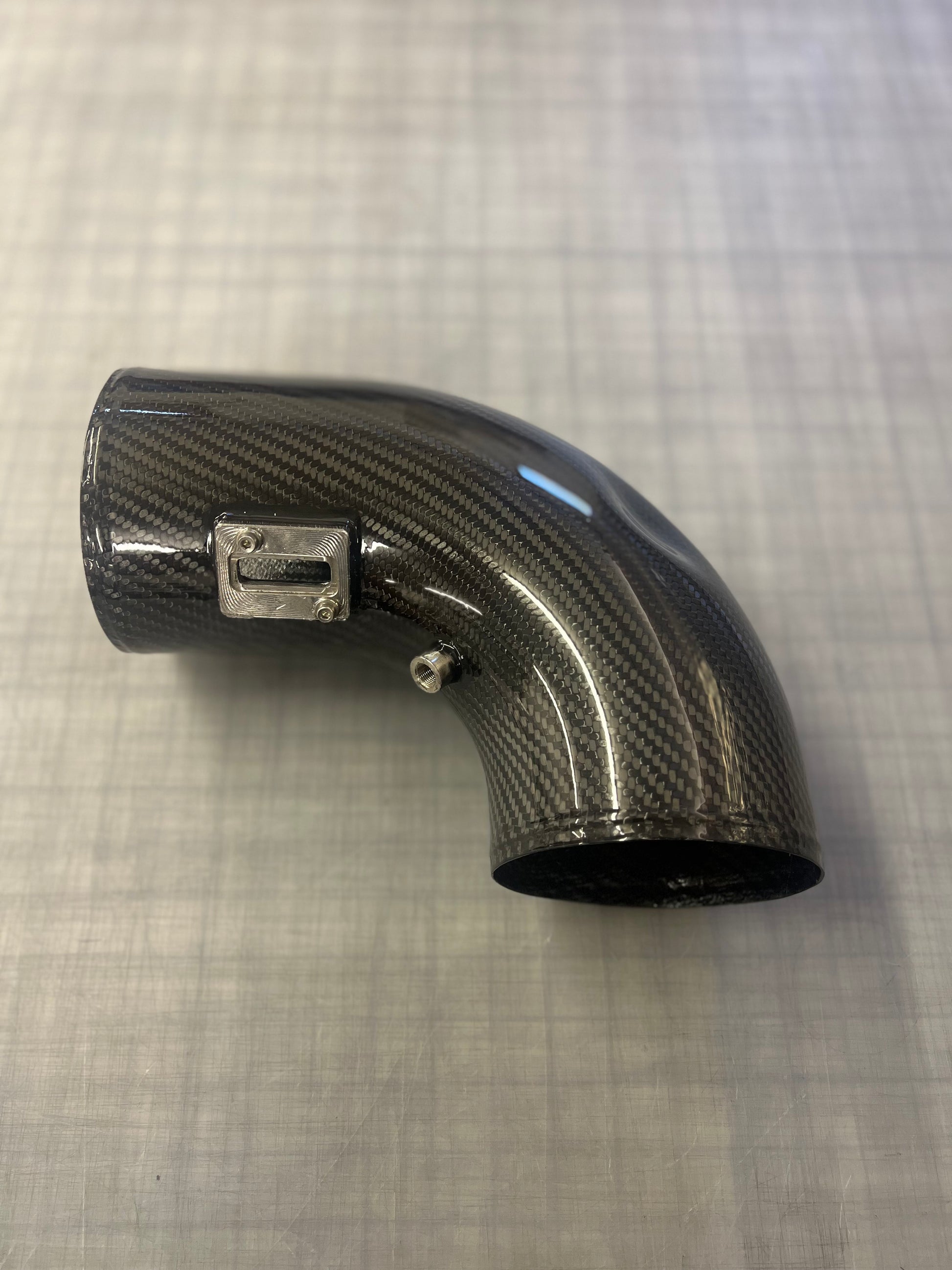 Carbon fiber elbow pipe on a textured gray background