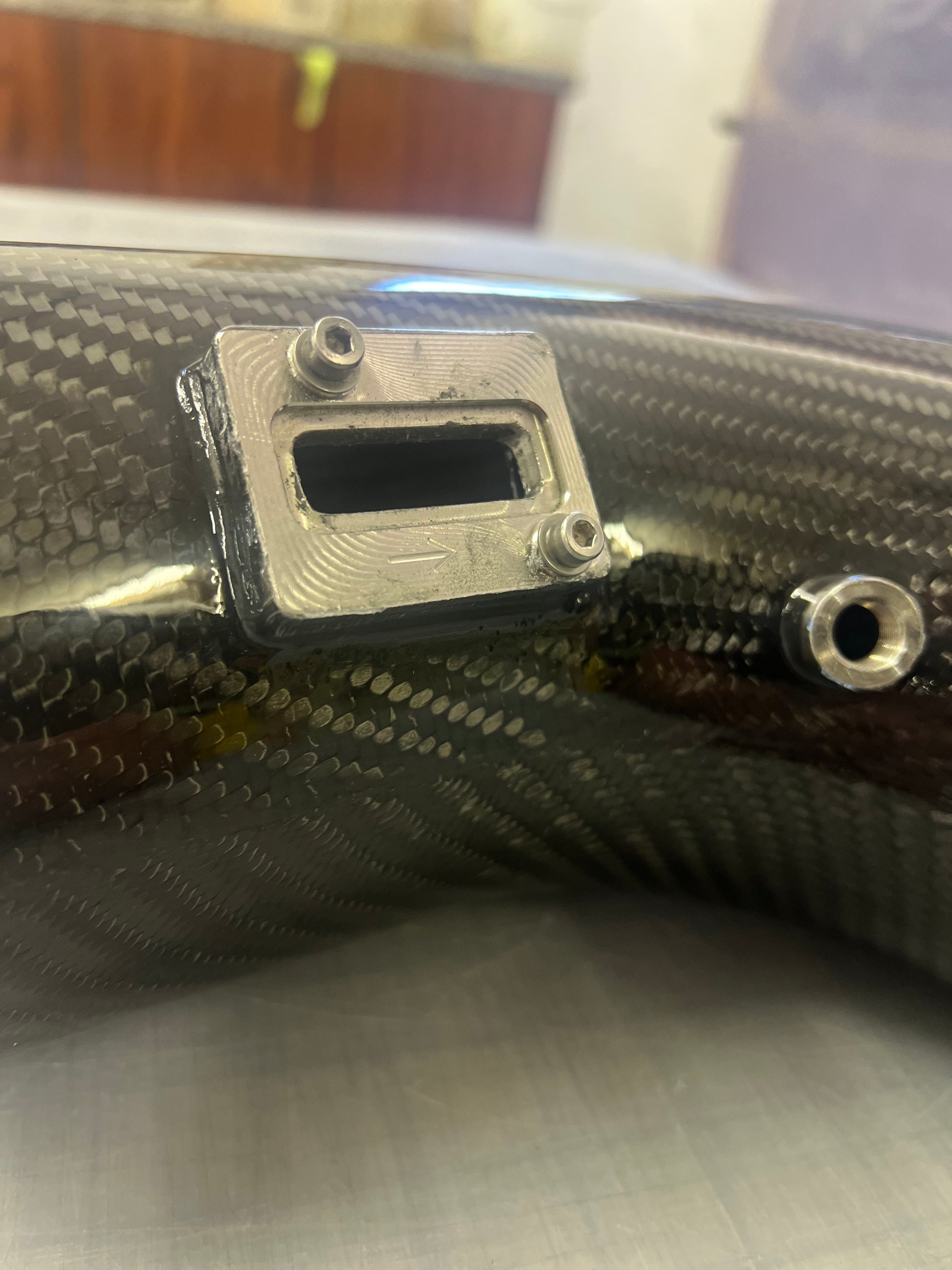 Close-up of a carbon fiber component with metal fitting and screws.