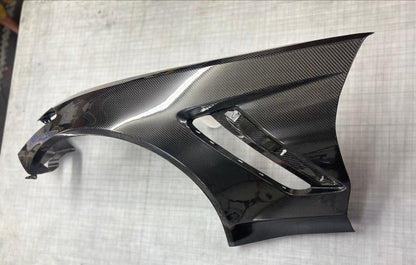 Carbon fiber car part on a white surface with a grid pattern
