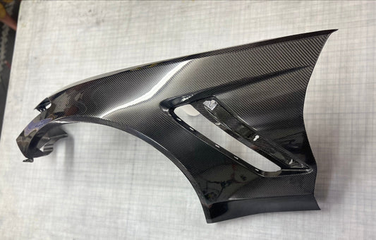 Carbon fiber car part on a white surface with a grid pattern