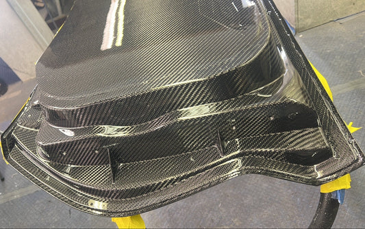 Carbon fiber car part on a stand with a blurred indoor background
