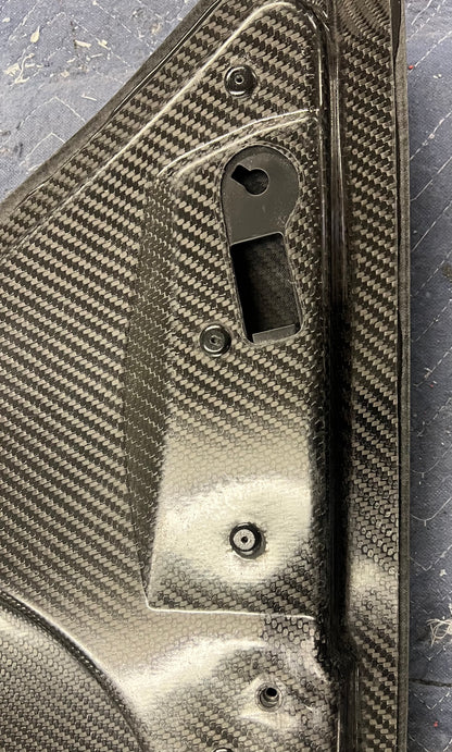 Close-up of a textured metal object with rivet holes on a carbon fiber surface background