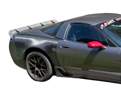 A dark gray carbon-fiber wrapped sports car shown from a rear three-quarter angle against a white background, featuring a black spoiler, black multi-spoke wheels, and a bright red side mirror.