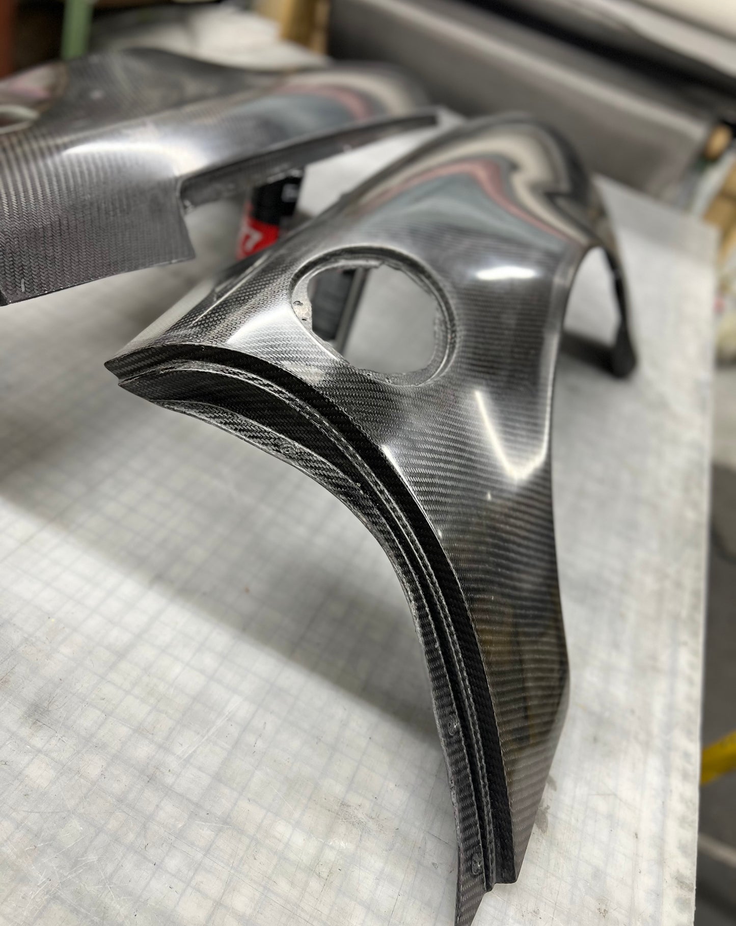 A pair of custom carbon fiber body panels with a glossy woven texture, displayed on a white grid work surface.